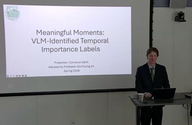Cameron at the podium beside the title slide: Meaningful Moments, VLM-Identified Temporal Importance Labels